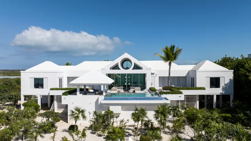 A white villa with a pool, surrounded by palms and tropical planting under a blue sky