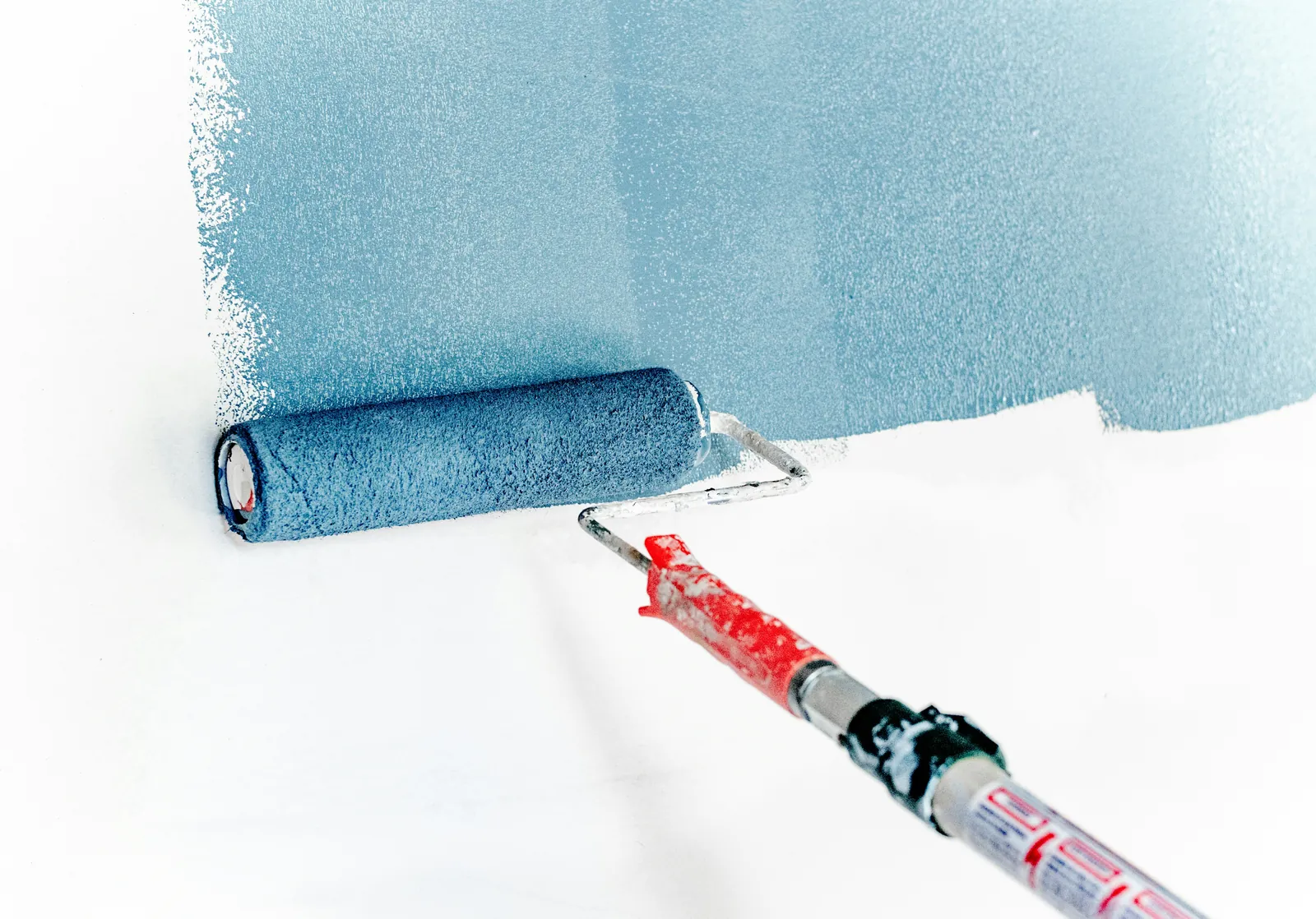 A paint roller laying a fresh coat of pale blue paint over a white wall