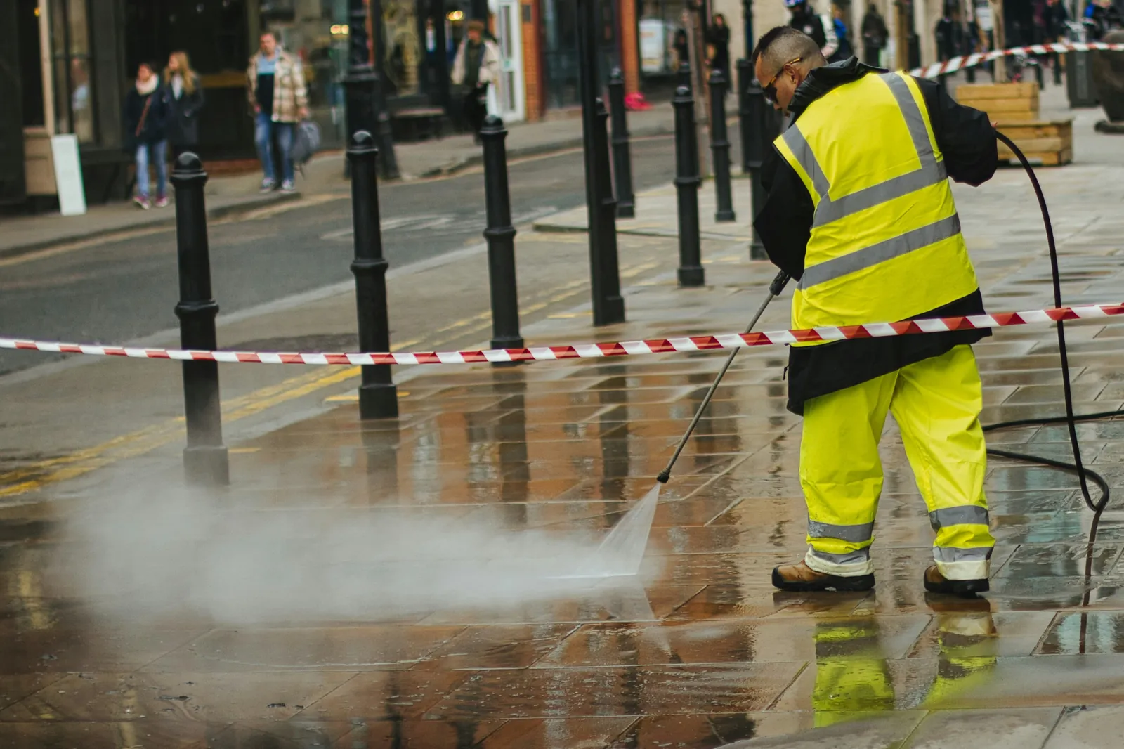 A worker in high-visibility gear cleaning paving with a pressure washer