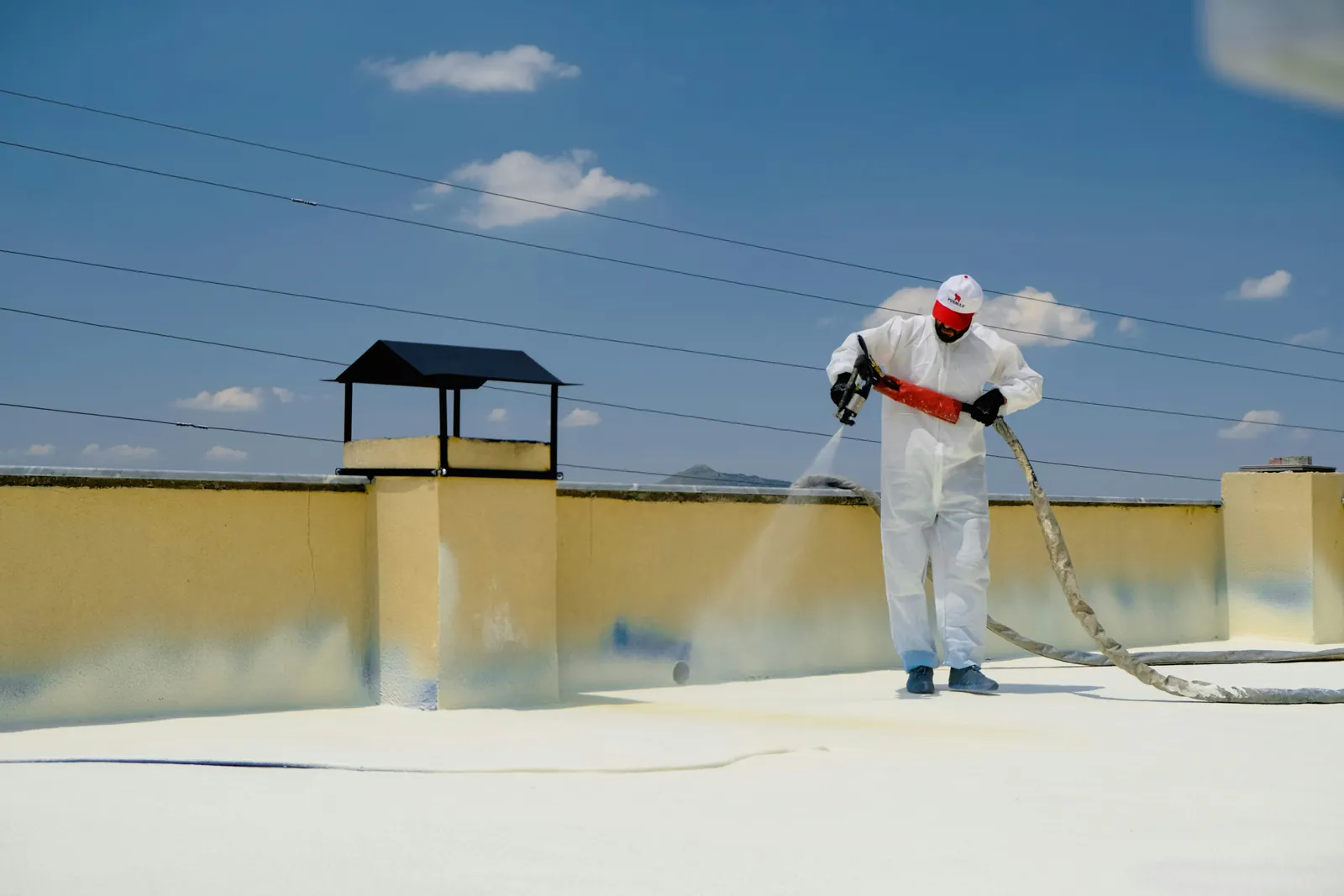 A worker in a white protective suit spraying a light coating onto a flat roof