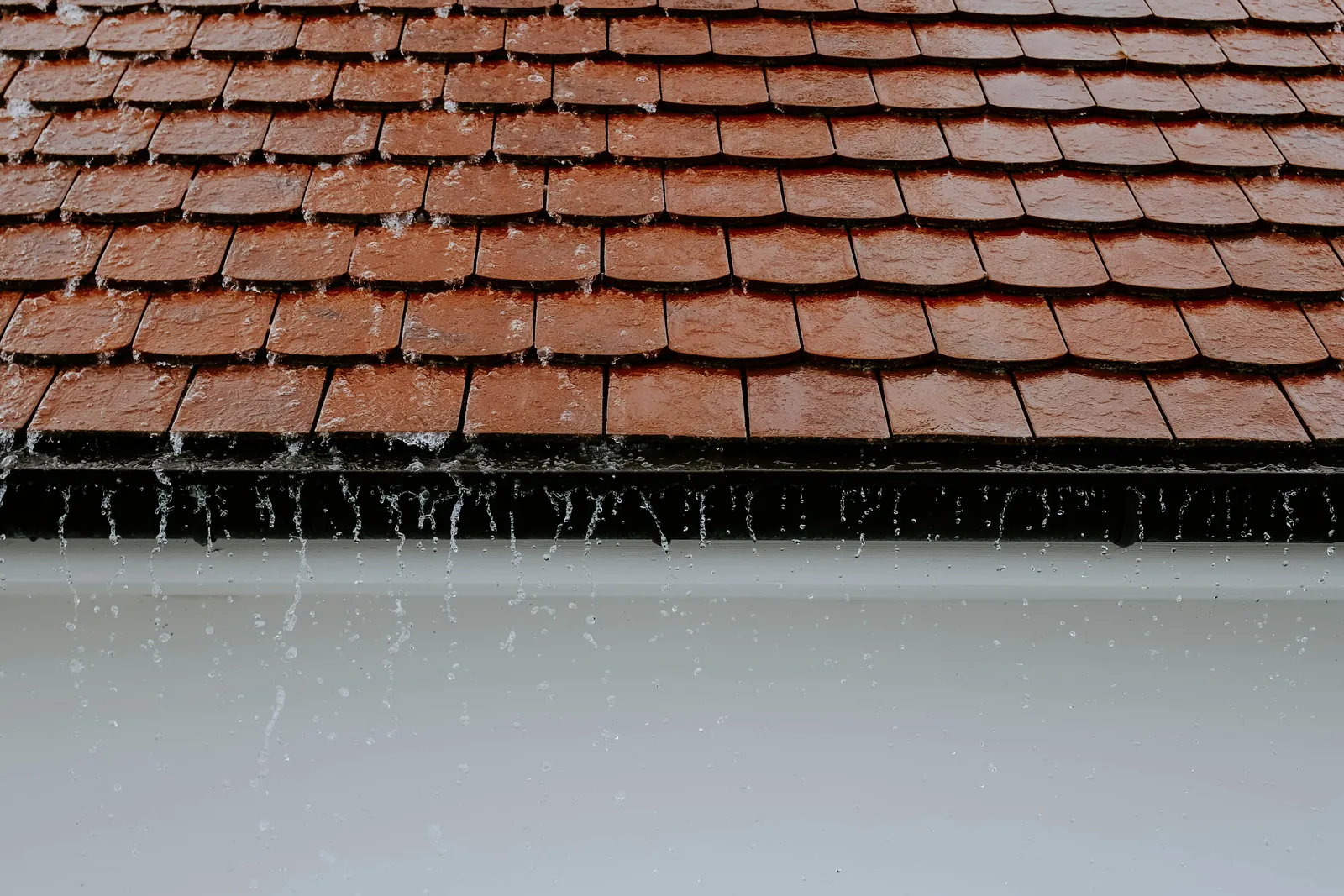 Rainwater running off a tiled roof edge above a white wall