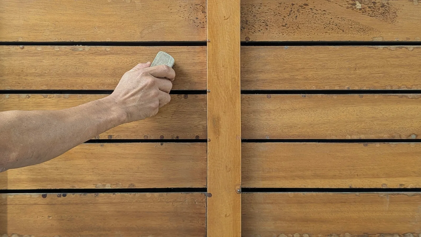 A hand sanding horizontal wooden slats with a sanding block